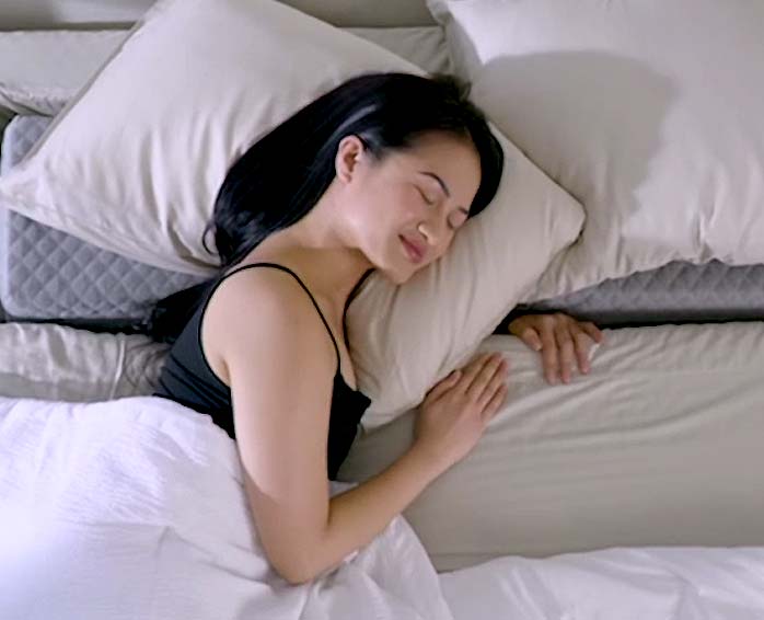 A female sleeper with her arms and shoulders in the Comfort Channel of the SONU mattress with cream sheets.