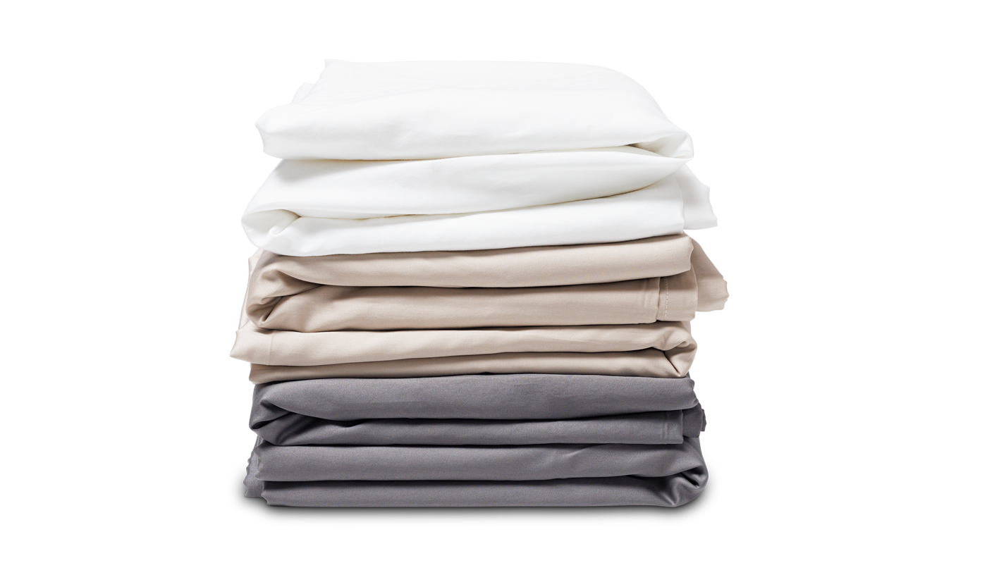 The SONU Sleep System's custom made cooling sheets, folded & stacked in different colors. They are white, cream and slate, from top to bottom.
